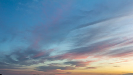 Vibrant hues of orange and pink blend with soft blue and gray clouds as the sun sets creating a...