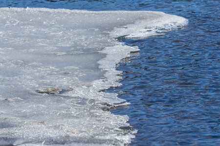 Melting ice meets flowing water at the riverbank showcasing a blend of blue hues with white ice...