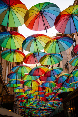 A collection of brightly colored umbrellas hangs overhead in a narrow street, casting a cheerful ambiance as the light dims during dusk hours.の写真素材