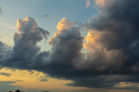 Expansive sky features dramatic clouds with golden tips as the sun sets creating a beautiful contrast against the deepening blue of the evening.の写真素材