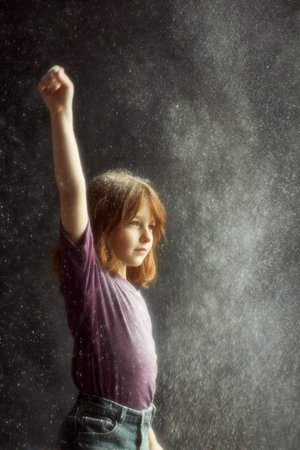 A child stands in a kitchen raising one arm high while flour is sprinkled into the air. Sunlight filters through a window creating a bright atmosphere.の素材