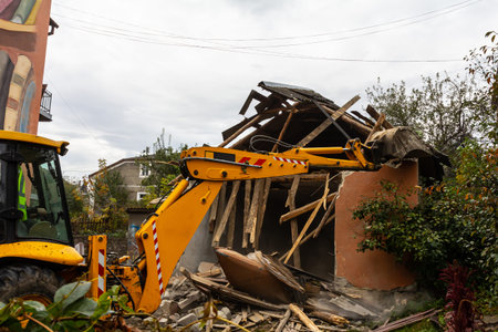 A construction vehicle is actively tearing down a dilapidated structure, scattering debris around an...