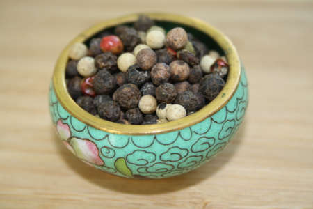 peppercorns in a ceramic plate on a wooden background. Space of your text.