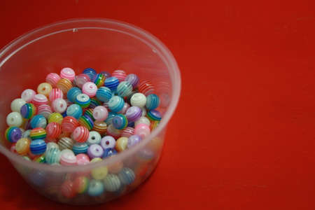 Beads in a box of different colors. Space for text. Red background.の写真素材