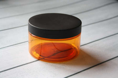 An orange plastic jar with a black lid from under the cosmetic product. Wooden background.の写真素材