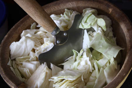 A knife for chopping cabbage with a wooden handle. Sliced cabbage in a wooden bowl. Culinary background.の写真素材