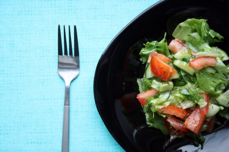 Salad of Frieze, tomatoes and cucumbers with olive oil in a black plate on a blue background.の写真素材