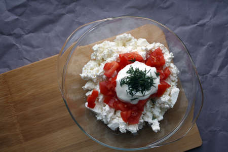Cottage cheese, tomatoes, dill and sour cream in a bowl. Space for text.