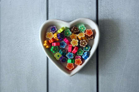 Multicolored beads in the form of flowers. Heart shaped plate on a wooden background.