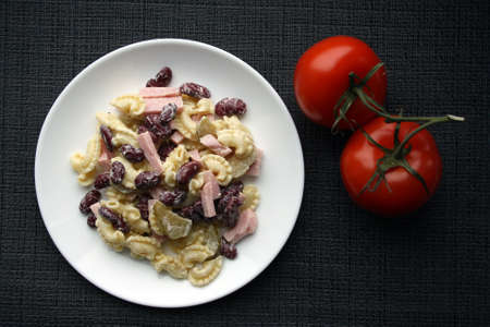Salad of pasta, ham, beans and pickled cucumbers. Belgian cuisine. In white plate on gray background.の写真素材