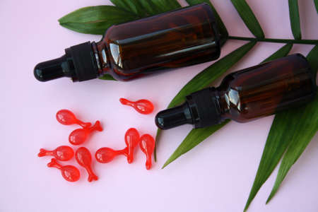 Brown bottles of cosmetic and essential oils, aromatherapy, natural cosmetics. Pink capsules with cosmetic oil for the face. Green leaf. Pink background.の写真素材
