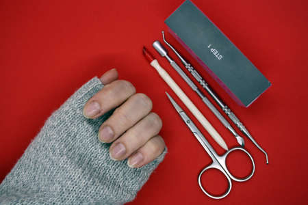 Female hand with bitten nails. Manicure tools. Red background.の写真素材