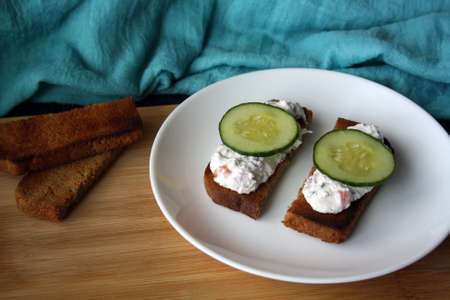 Cottage cheese dip with cucumber slices on black bread toast. Breakfast. Space for text.の写真素材