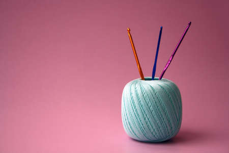 A ball of green threads and crochet hooks on a pink background.