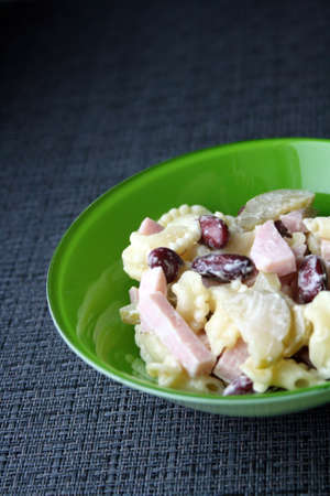 Salad of pasta, ham, beans and pickled cucumbers. Belgian cuisine. In green plate on gray background.の写真素材