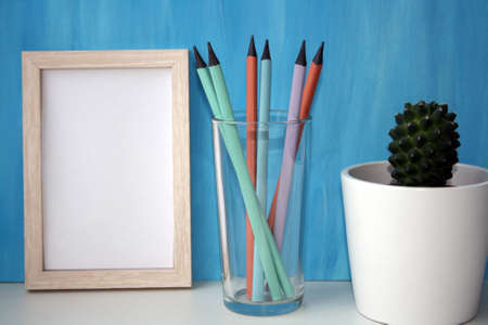 Mockup frame and plant in a pot by a blue wall. Pencils in a glass. Copy space.の写真素材