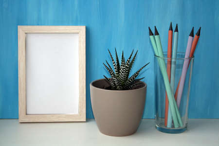 Mockup frame and plant in a pot by a blue wall. Pencils in a glass. Copy space.の写真素材