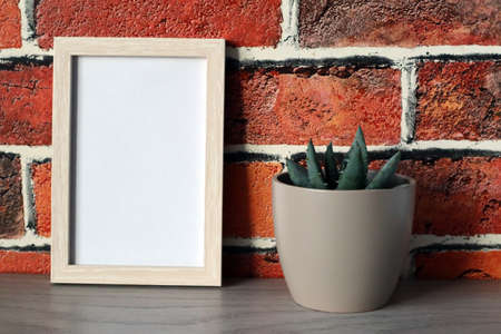 Mock up white frame with gray flower pot with succulent on brick wall background. Space for text.