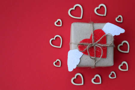 Craft gift box with red heart with white wings and craft ribbon on red background. For celebrate. Valentines day conception. Top view.の写真素材