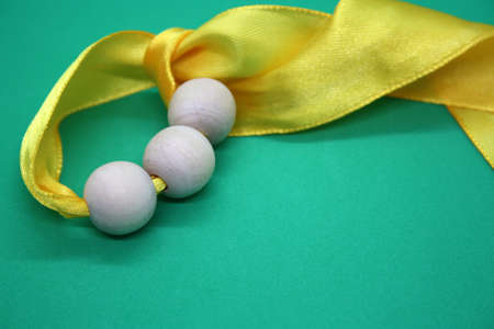 Wooden beads and yellow ribbon on a green background. Space for text.の写真素材