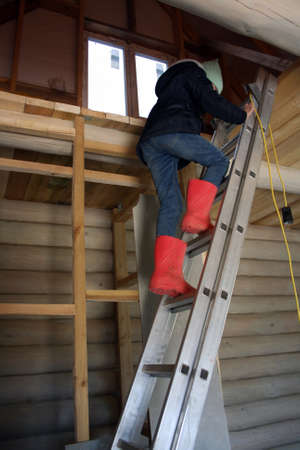 A child in red boots climbs the stairs in an unfinished log house.の写真素材