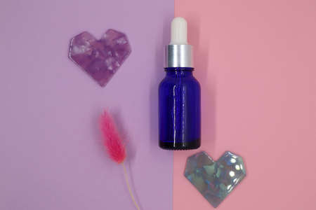 Container, cosmetic blue bottle, heart and dried flowers on a pink background. Blank label for...