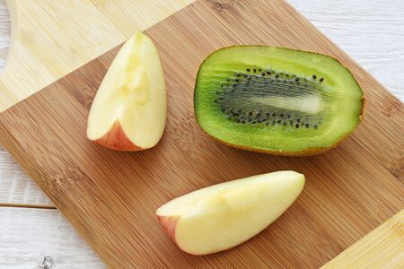 Half kiwi and an apple on a chopping board close upの写真素材