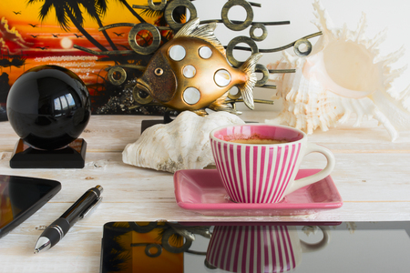 Mobile phone, tablet, coffee cup, seashell and fish on a wooden tableの写真素材