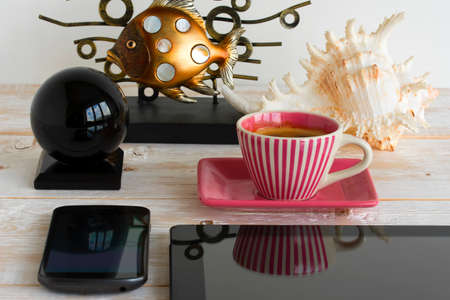 Mobile phone, tablet, coffee cup, seashell and fish on a wooden tableの写真素材