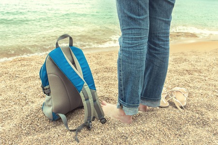 Goodbye summer concept. Girl is standing by the sea. Backpack in the sandの写真素材