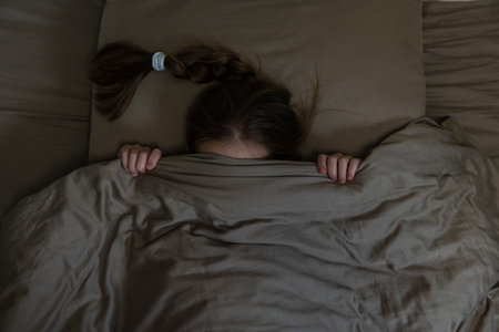 Girl with dark hair hides in bed with fear. high qualityの写真素材