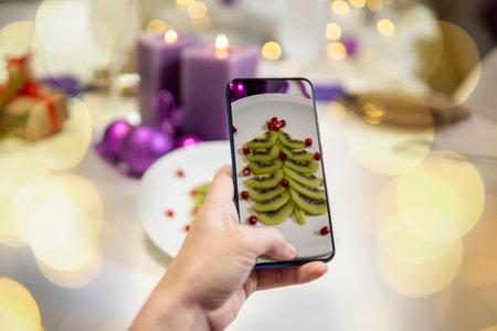 Girl's hand takes pictures of Christmas table. kiwi and pomegranate in the shape of a christmas tree on a platter. high qualityの写真素材