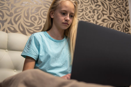 Teenage girl with blond hair working on laptop in bed. high qualityの写真素材