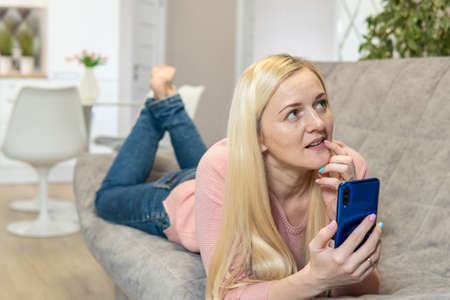 Blonde girl lie on the couch and look into the phone. high qualityの写真素材