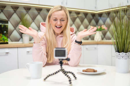 Girl blogger with blonde hair doing video on action camera in the house