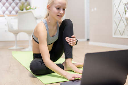 young attractive girl is engaged in fitness at home and looks at the laptop. quarantine fitness...