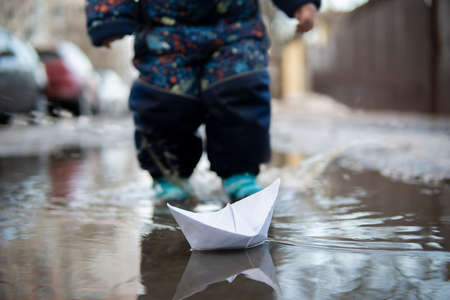 Little boy plays with paper ships in a spring puddleの写真素材