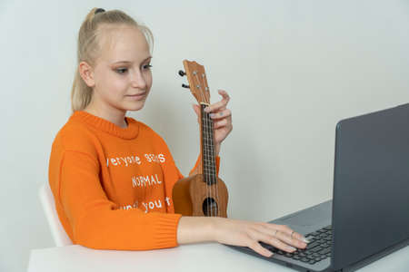 Teenage girl learns to play the ukulele and looks into her laptop.の写真素材