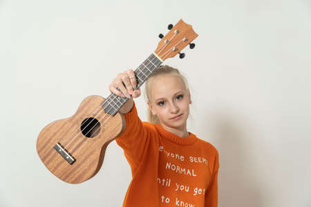 teen girl holding a guitar ukulele and laughing on a light background.の写真素材