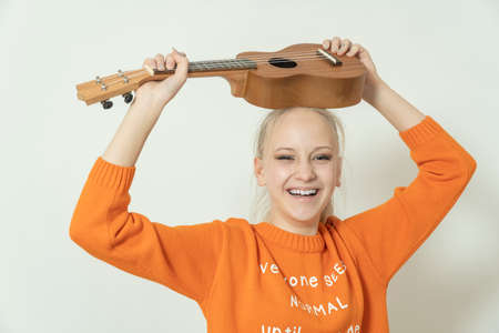 teenage girl with blond hair with guitar on gray background.