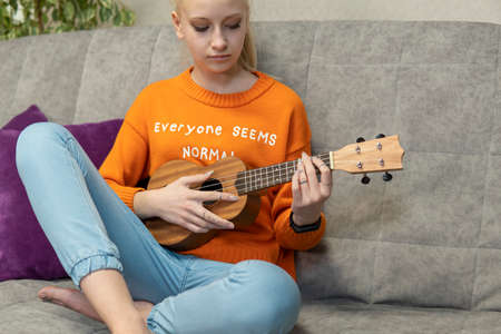 Teenage girl learns to play the ukulele and looks into her laptop