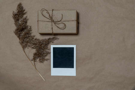 Gift box wrapped in craft paper with a reed stalk, dried pampas grass on a dark background. New fashionable home decor, copy space. Vertical photo.の写真素材