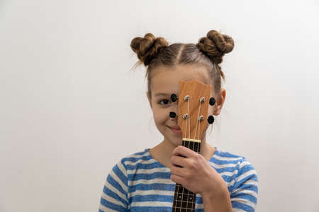 Girl with dark hair playing guitar ukulele on a light background
