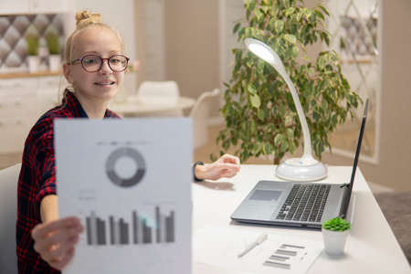 Blonde girl with glasses work on a laptop and show graphs. Home-school concept. high qualityの写真素材