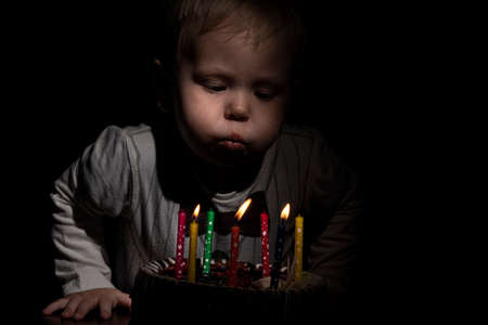 Birthday. A little sweet boy blows out candles on the stoke. dark background.の写真素材