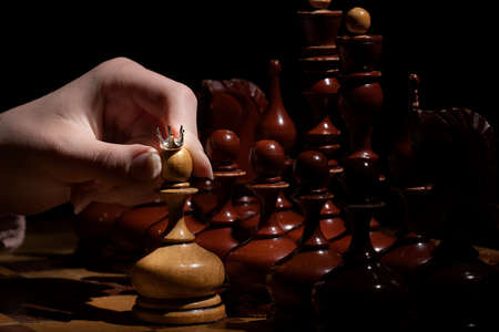 female hand holds a pawn with a crown on a dark background. old chess. business concept.
