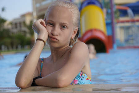 Teenage girl with blond hair bored in children's pool.の写真素材