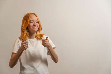 Portrait of a teenage girl with red hair and a white T-shirt laughing at the light background.の写真素材