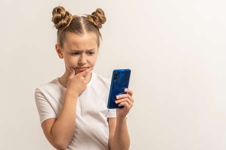 Girl with dark hair and white T-shirt watch phone on light background.