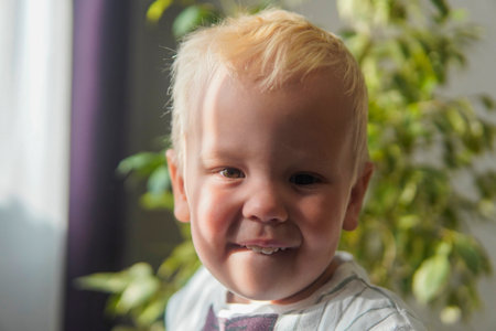 little boy with blonde hair laughing in the sun at home.